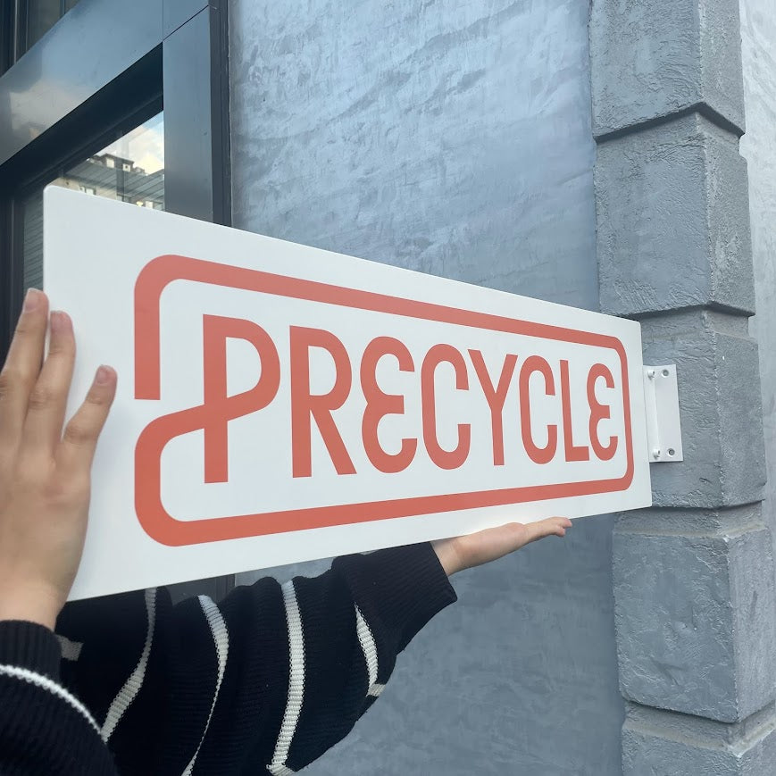 Sokak cephesine monte edilmiş dikdörtgen metal tabela, dış mekanda dikkat çekici görünüm sunuyor.

