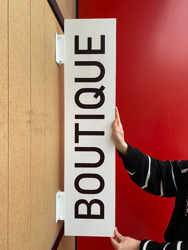 Siyah zemin üzerine beyaz yazı baskısı olan dikdörtgen formda tabela.